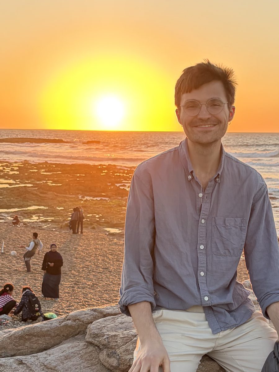 Zach sitting on a rock at the beach at sunset